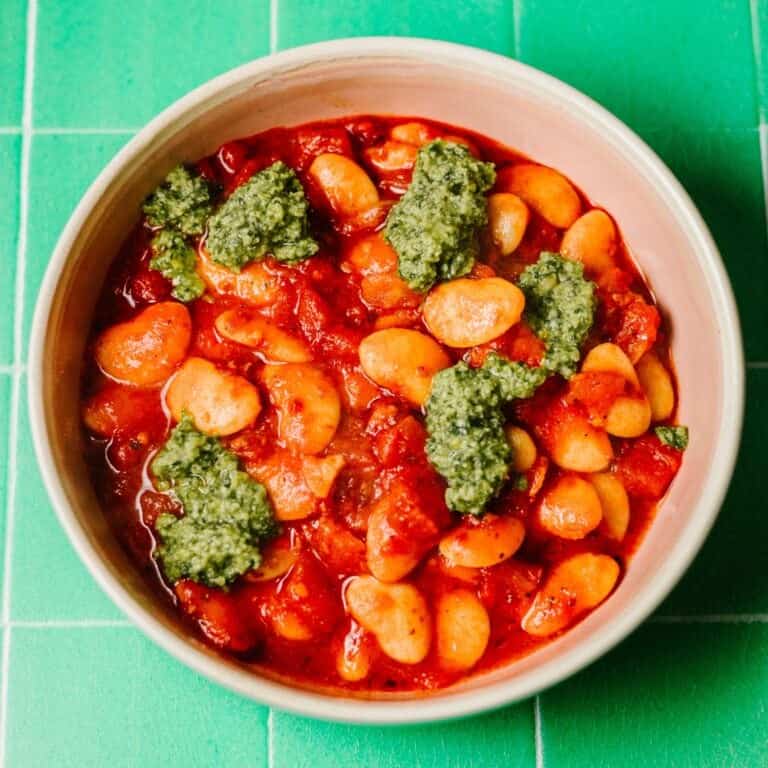 A bowl of Spicy Nduja Tomato Butter Beans garnished with fresh basil pesto on top. Hearty stew, easy midweek recipe.