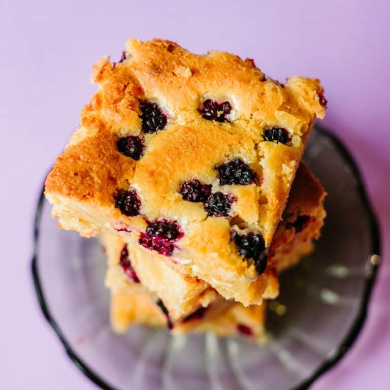 A close-up of gooey Blackberry White Chocolate Blondies, featuring golden-brown edges, a fudgy centre studded with juicy blackberries, and chunks of white chocolate. Blondie recipe.