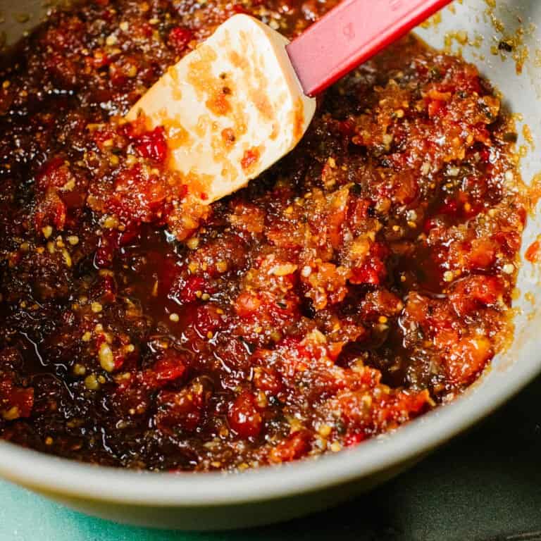 A jar of homemade sweet chilli jam, surrounded by fresh chillies, onions, and garlic, ready to enjoy.