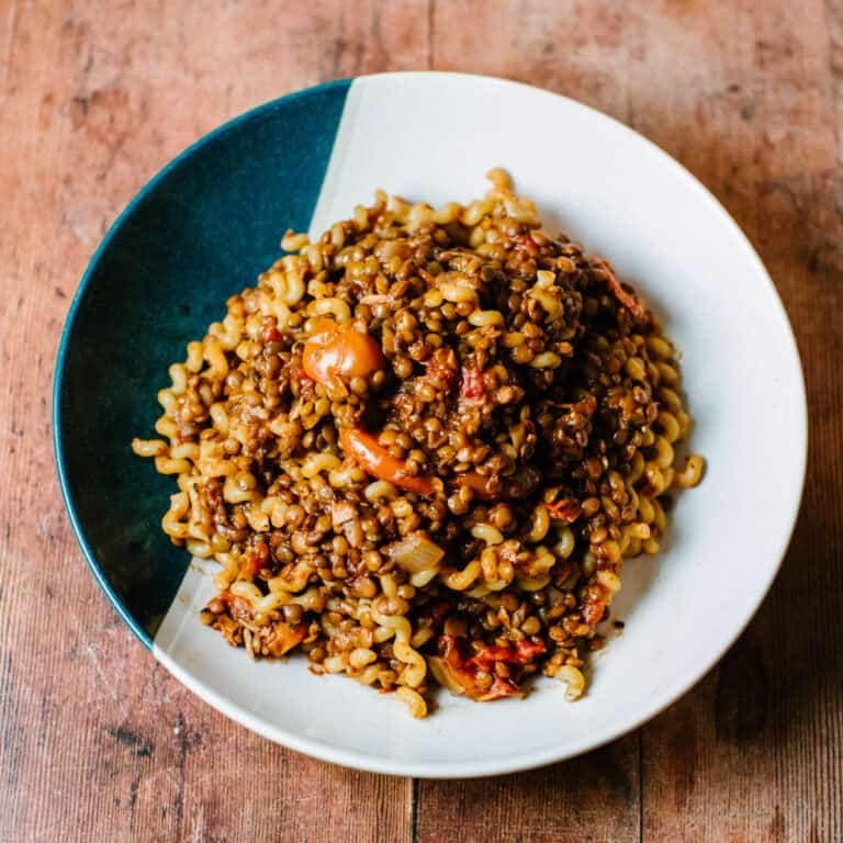 A hearty bowl of green lentil bolognese served over pasta, garnished with fresh basil and grated parmesan