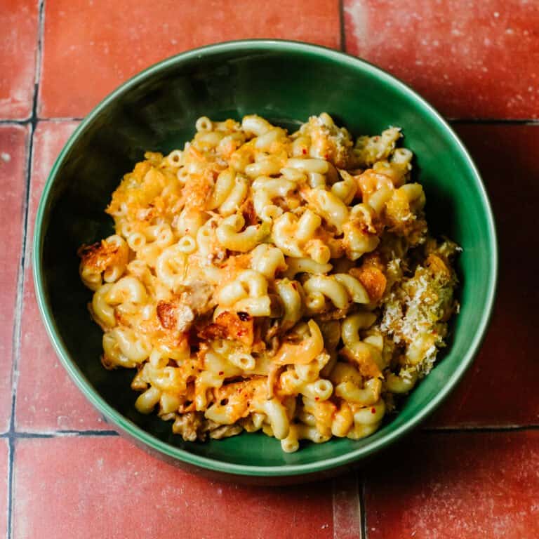 A vibrant, golden-brown kimchi mac and cheese topped with crispy panko breadcrumbs, garnished with fresh green onions, served in a rustic baking dish.