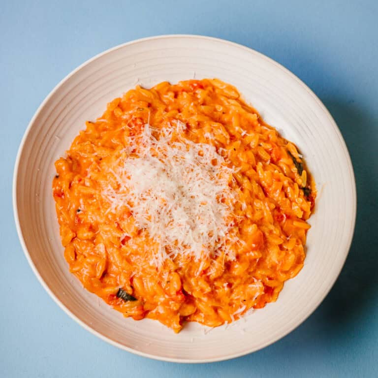 Gochujang Tomato Orzo with Sausage recipe topped with grated parmesan on a pale blue background