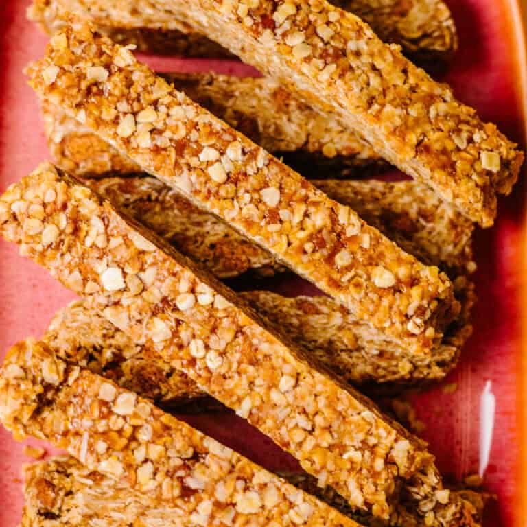 Square featured image of chewy biscoff granola bars stacked neatly on a white plate, with visible oat texture and golden biscuit crumbs